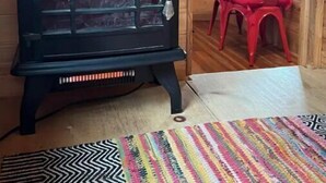 Interior de madera con un estufa de leña negra, sillas rojas y una alfombra colorida.