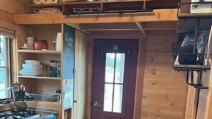 Cocina compacta con encimera de madera, estufa y una pequeña mesa con una silla.