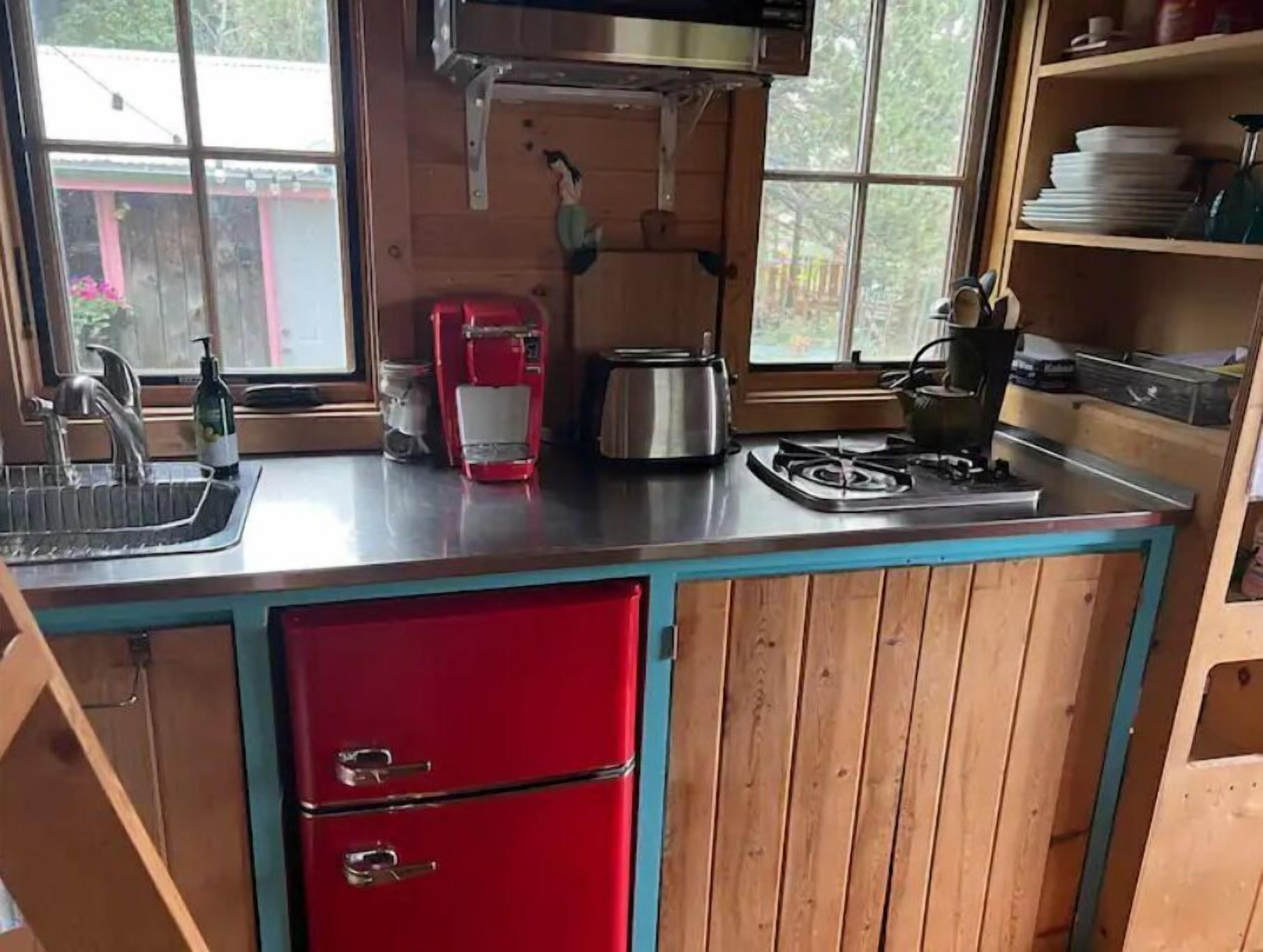 Una cocina compacta con un lavamanos, una cafetera roja, una estufa y armarios de madera.