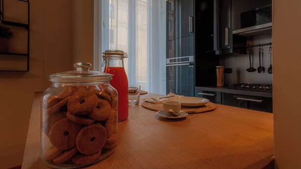 Una cocina con una mesa de madera, un tarro de cristal con galletas, una botella roja y una estufa moderna.