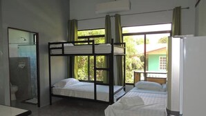 A room with bunk beds, a desk, a chair, a toilet, and a window with curtains. - Paraíso Chamán 5 (Uvita)