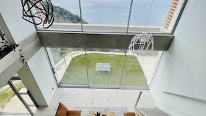 A modern living room with a sofa, coffee table, and two armchairs. A large window offers a view of a grassy area and a body of water.