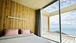 A bedroom with a large bed, wooden panel walls, a skylight, and a view of the sea.