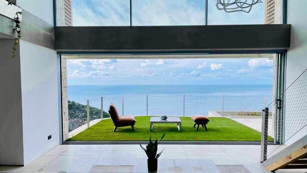 A modern interior with a large glass window overlooking a grassy area and the sea.