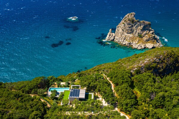 Una propiedad costera con piscina, paneles solares y un promontorio rocoso en el mar.