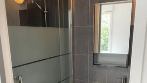 Ein modernes Badezimmer mit einer gläsernen Dusche, einem weißen Waschbecken und einem Spiegel darüber.