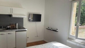 Eine kompakte Küche mit Flachbildfernseher, einer kleinen Ablage und einem Fenster mit Blick ins Grüne.