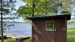 Pieni puinen mökki, jossa on savupiippu, ikkuna ja laiturin jatke, joka ulottuu järveen.