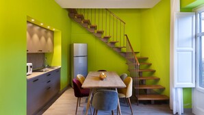 A modern kitchen with a wooden table and chairs, a refrigerator, and a staircase against a green wall.