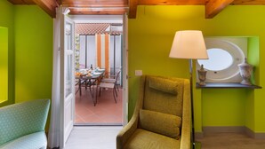 A room with a green wall, a wooden ceiling, a green sofa, a chair, a table with chairs, and a window with a lamp.