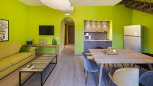 A modern kitchen with a microwave, refrigerator, and wooden cabinets. There is a dining table with chairs and a sofa in the living area.