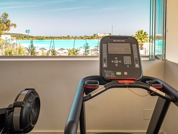 Una caminadora con pantalla digital y panel de control, con vistas a una playa con sombrillas y palmeras.