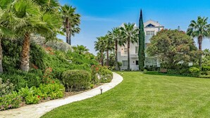 Un jardín bien cuidado con un camino curvo que lleva a una casa moderna con un amplio ventanal y un balcón.
