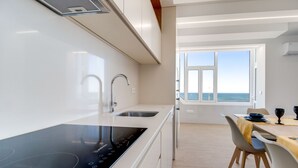 A modern kitchen with a built-in stove, a sink, and a window overlooking the sea. - Modern 3BD Ocean View Apartment (Póvoa de Varzim)