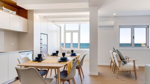 A modern dining area with a view of the sea, white cabinetry, and a wooden floor. - Modern 3BD Ocean View Apartment (Póvoa de Varzim)