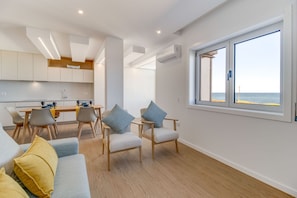 A modern living room with a sofa, two armchairs, a dining table with chairs, and a large window with a view of the sea. - Modern 3BD Ocean View Apartment (Póvoa de Varzim)