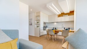 A modern kitchen with white cabinets, a dining area with chairs, and a sofa with cushions. - Modern 3BD Ocean View Apartment (Póvoa de Varzim)