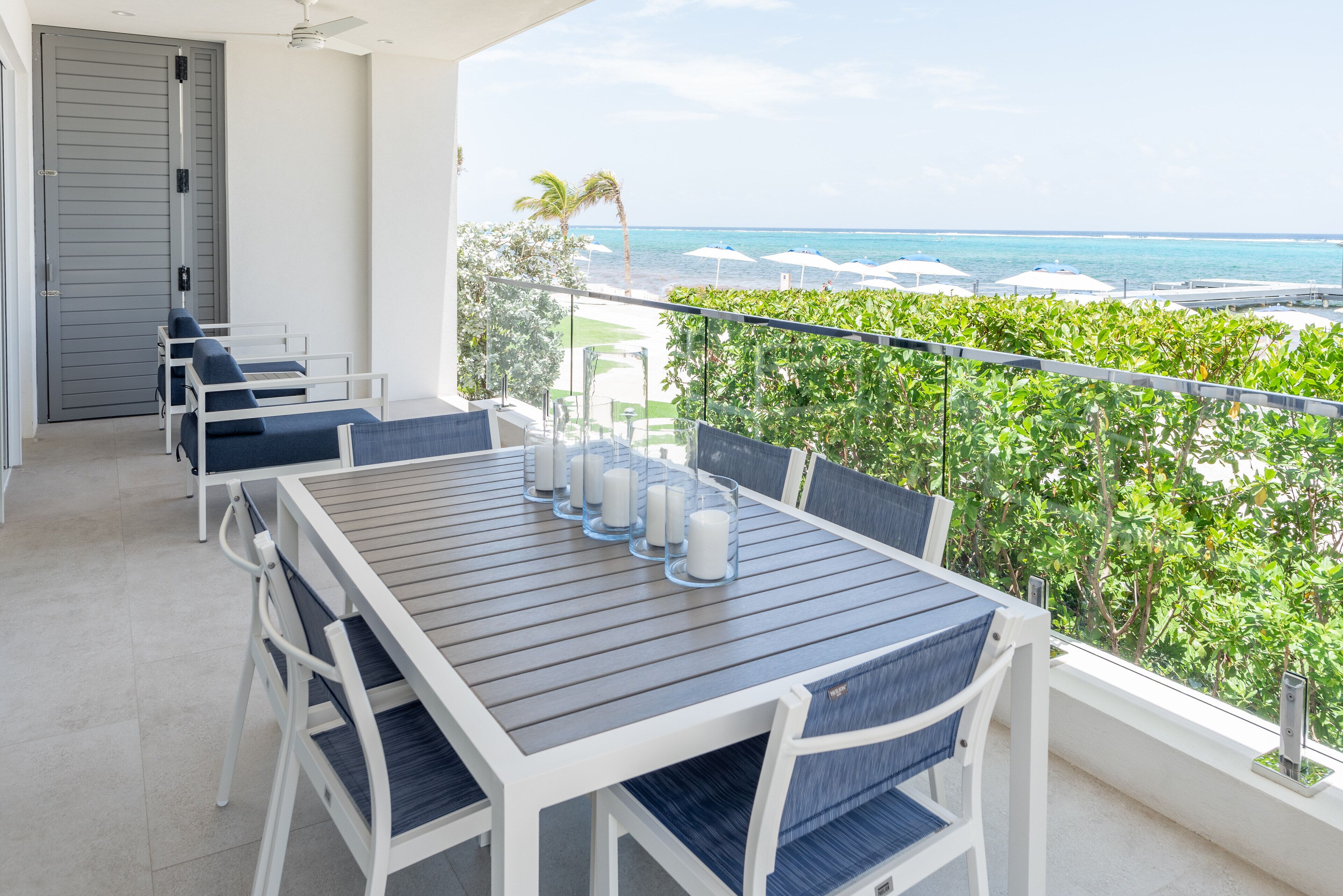 Un balcon avec une table et des chaises, donnant sur une plage et l’océan.