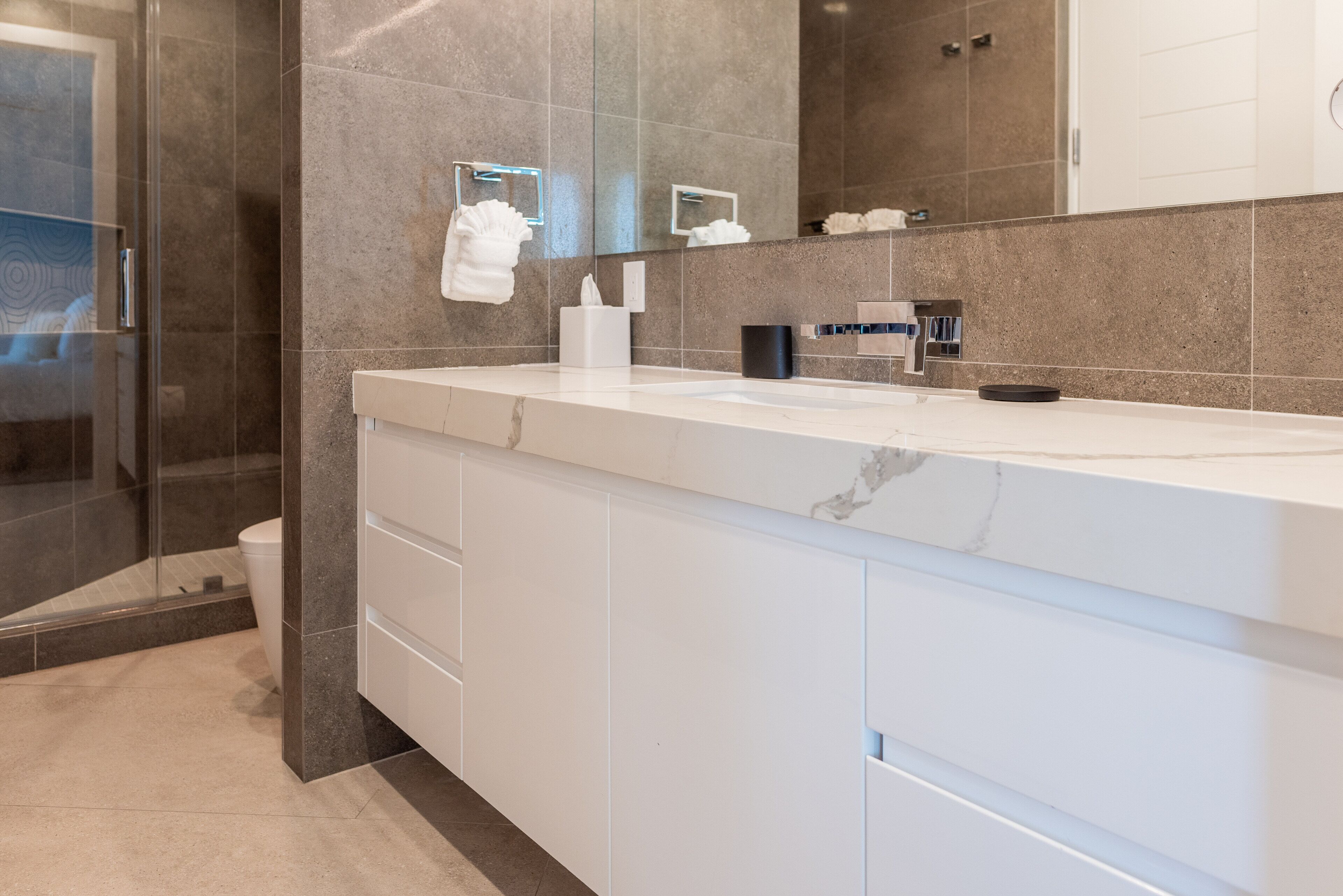 A modern bathroom with a glass shower enclosure, a white vanity with a marble countertop, and a large mirror.