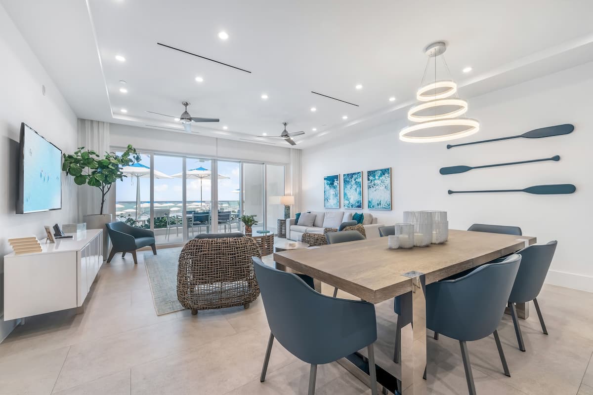 A modern, well-lit dining area with a wooden table, blue chairs, and a ceiling fan.