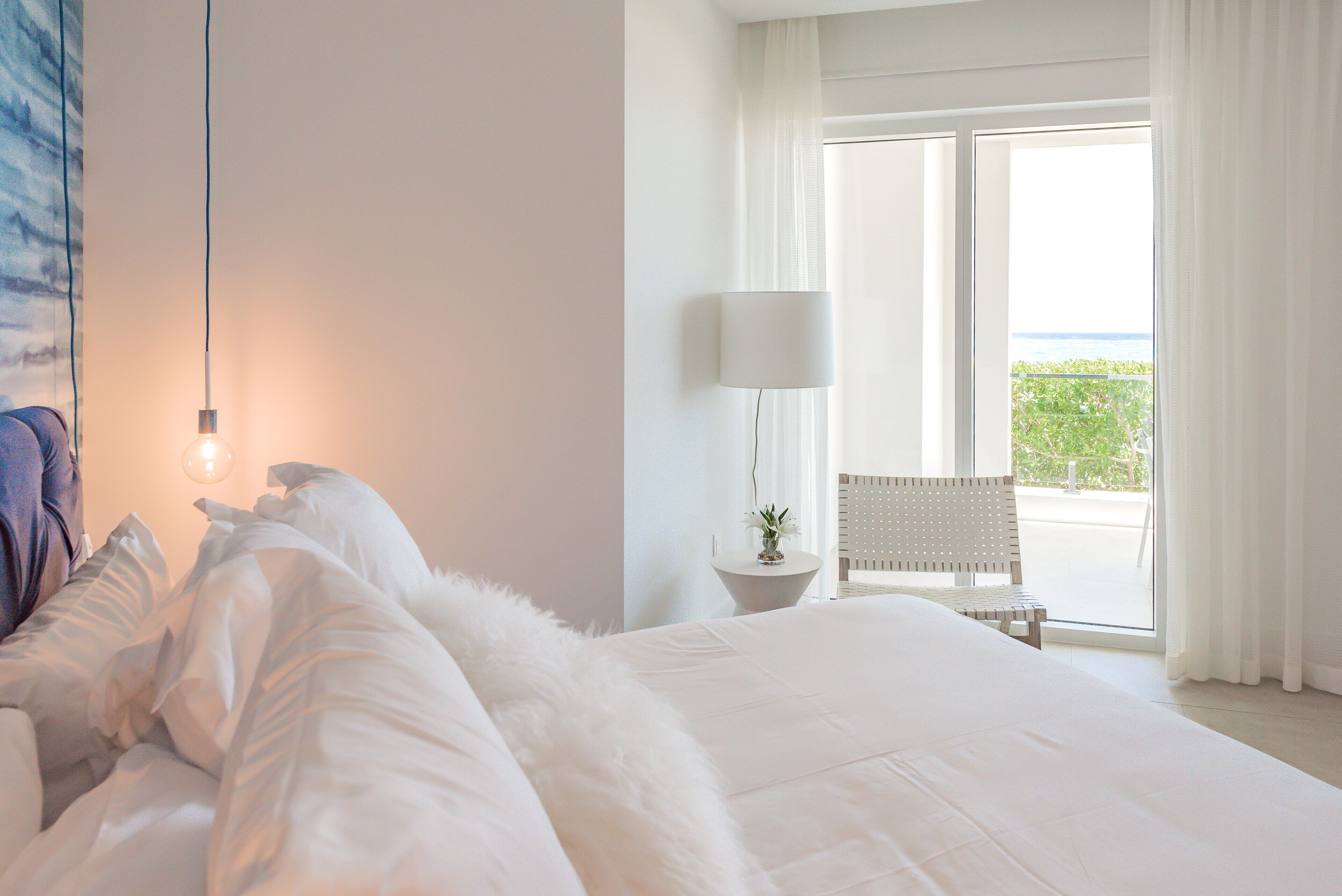 Quarto de hotel com uma cama grande, abajur, cadeira e vista para o exterior.