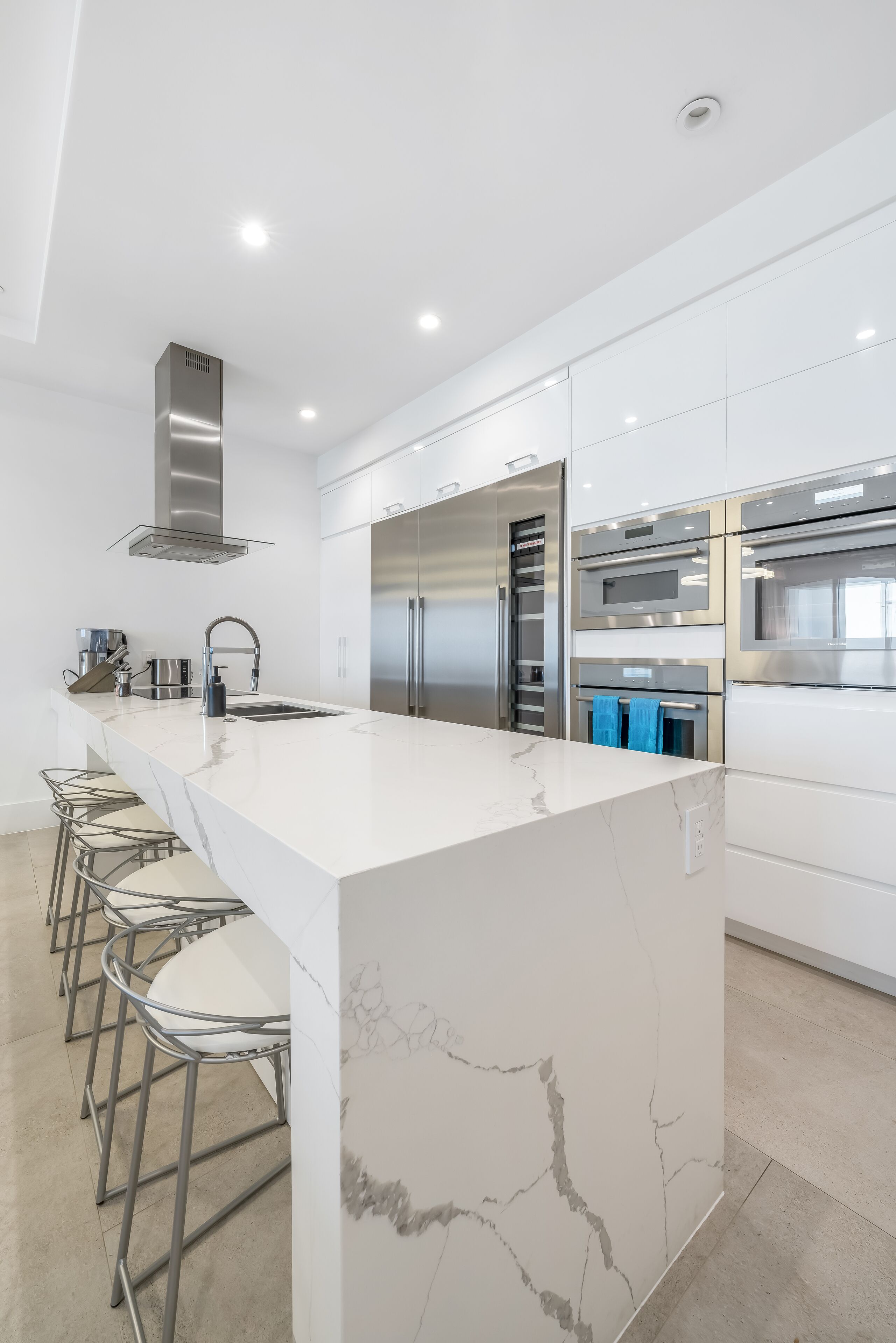 A modern kitchen with a large island, stainless steel appliances, and bar stools.