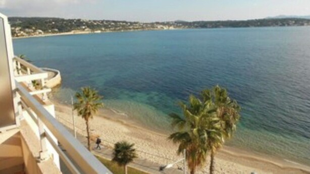 Blick auf die Küste vom Balkon aus, mit Strand, Palmen und blauem Himmel.