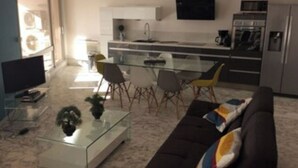 Ein modernes Wohnzimmer mit einem Glastisch, einem dunklen Sofa und einem Fernseher.