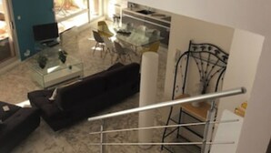 Ein modernes Wohnzimmer mit einem dunklen Sofa, einem Glastisch und einem Essbereich mit weißem Tisch und Stühlen.