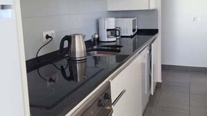 Eine Küche mit schwarzem Arbeitsplatz, einem Edelstahlkocher, einer weißen Mikrowelle und einer Kaffeemaschine.