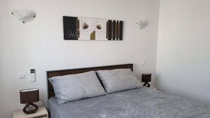 Ein Schlafzimmer mit einem Bett, zwei Nachttischen, einem Wandbild und einer Leuchte.