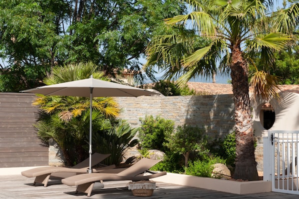 A patio with lounge chairs, a large umbrella, and a palm tree. - RESIDENCE MARINA ROSSA VILLA WITH GARDEN, 10 MINUTES FROM CALA ROSSA BEACH (Lecci)