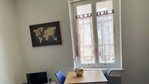 A room with a wooden table and four blue chairs, a world map on the wall, a TV on a white stand, and a window with decorative curtains. - 🌹🍾Superb studio 5 mins from cathedral 🥂 (Reims)