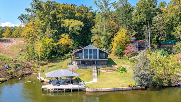 A lakeside cabin with a dock, surrounded by lush greenery and trees. - Lavish Lake Getaway W/180* Views+ Boat Dock (Knoxville)
