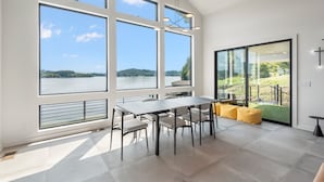 A spacious room with large windows offering a view of a lake and hills. There is a dining area with a table and chairs. - Lavish Lake Getaway W/180* Views+ Boat Dock (Knoxville)