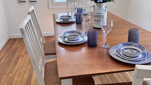 Une table à manger dressée avec de l’assiette bleue et blanche, un vase rempli de fleurs et une décoration en forme de roue de navire accrochée au mur.