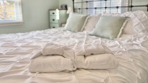 Un lit bien fait, avec du linge de lit et des serviettes blanches, une table de chevet avec une lampe et une fenêtre avec des stores.