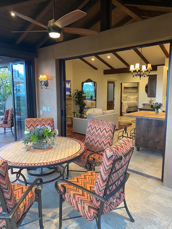 A dining area with a round table and chairs, a ceiling fan, and a view into a living room with a sofa and a dining table. - Beautiful Mediterranean Cottage on larger estate. (Santa Barbara)