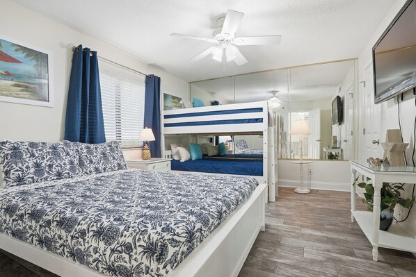 A bedroom with a bunk bed, a single bed, a ceiling fan, a TV, and a mirror.