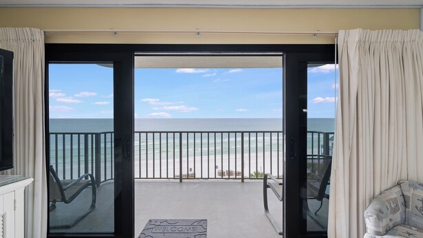 Un balcón con vista a la playa, una puerta con felpudo de bienvenida y una silla.