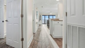 Un pasillo con puertas blancas, una zona de cocina con armarios blancos y vistas al exterior.