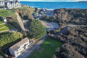 An aerial view of a coastal area with a parking lot, a large building, and a road curving through the landscape.