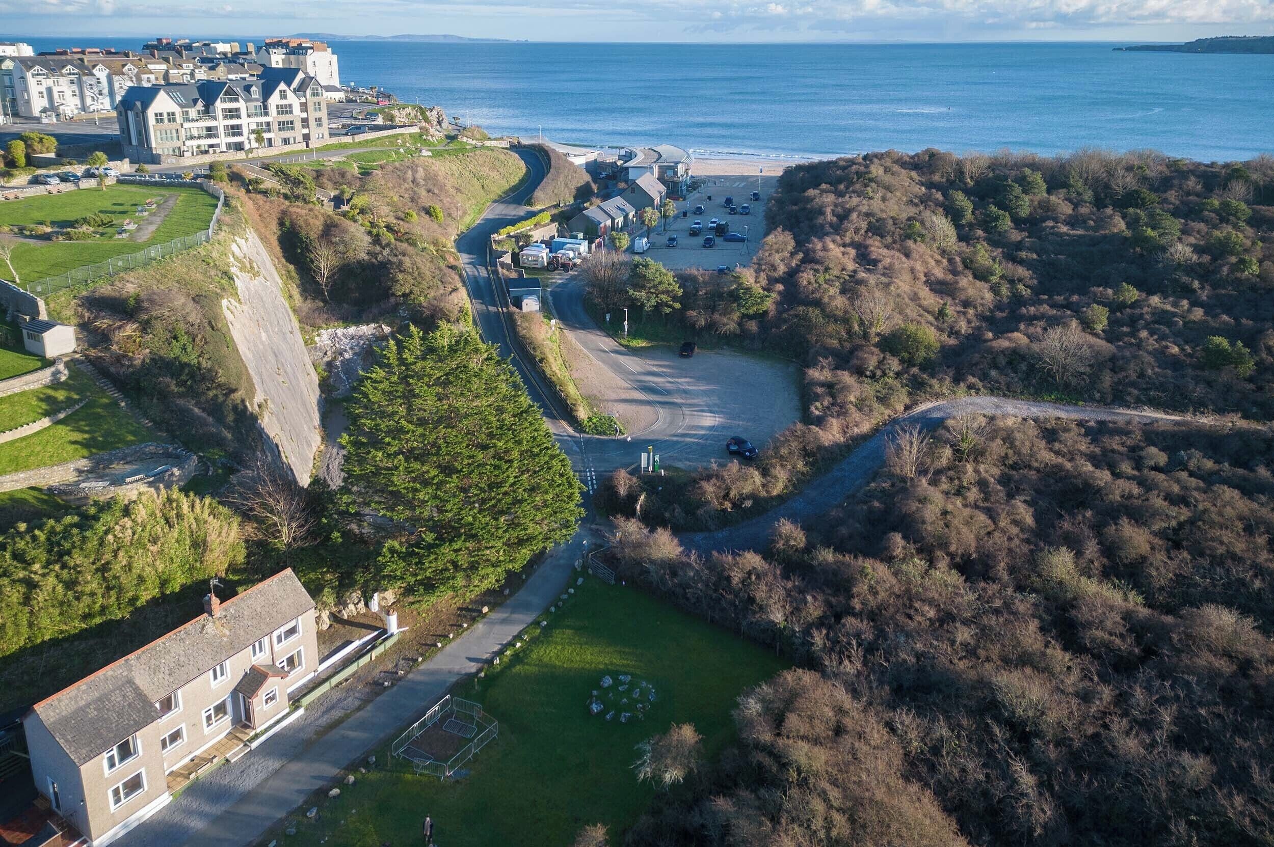 An aerial view of a coastal area with a large building complex, a parking lot, and a road leading to a beach.