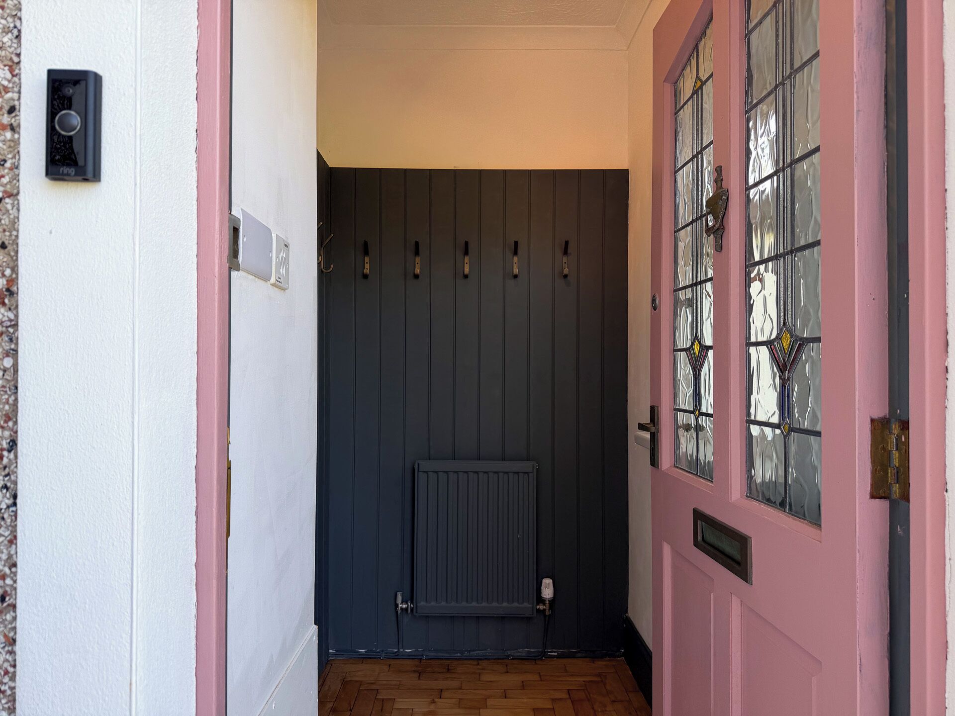 Un corridoio con una porta scura, un termosifone e una parete rosa.