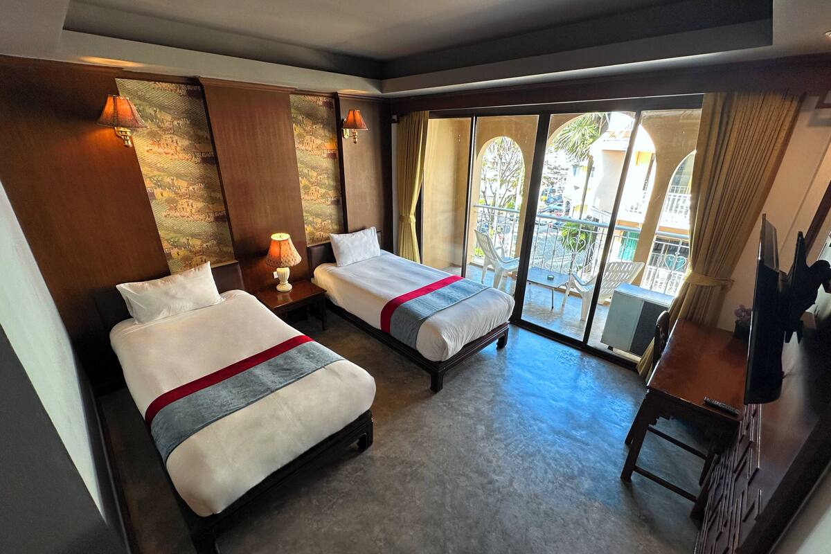 Ein Hotelzimmer mit zwei Betten, einem kleinen Tisch, einem Fernseher und einem Balkon mit Sitzgelegenheit.