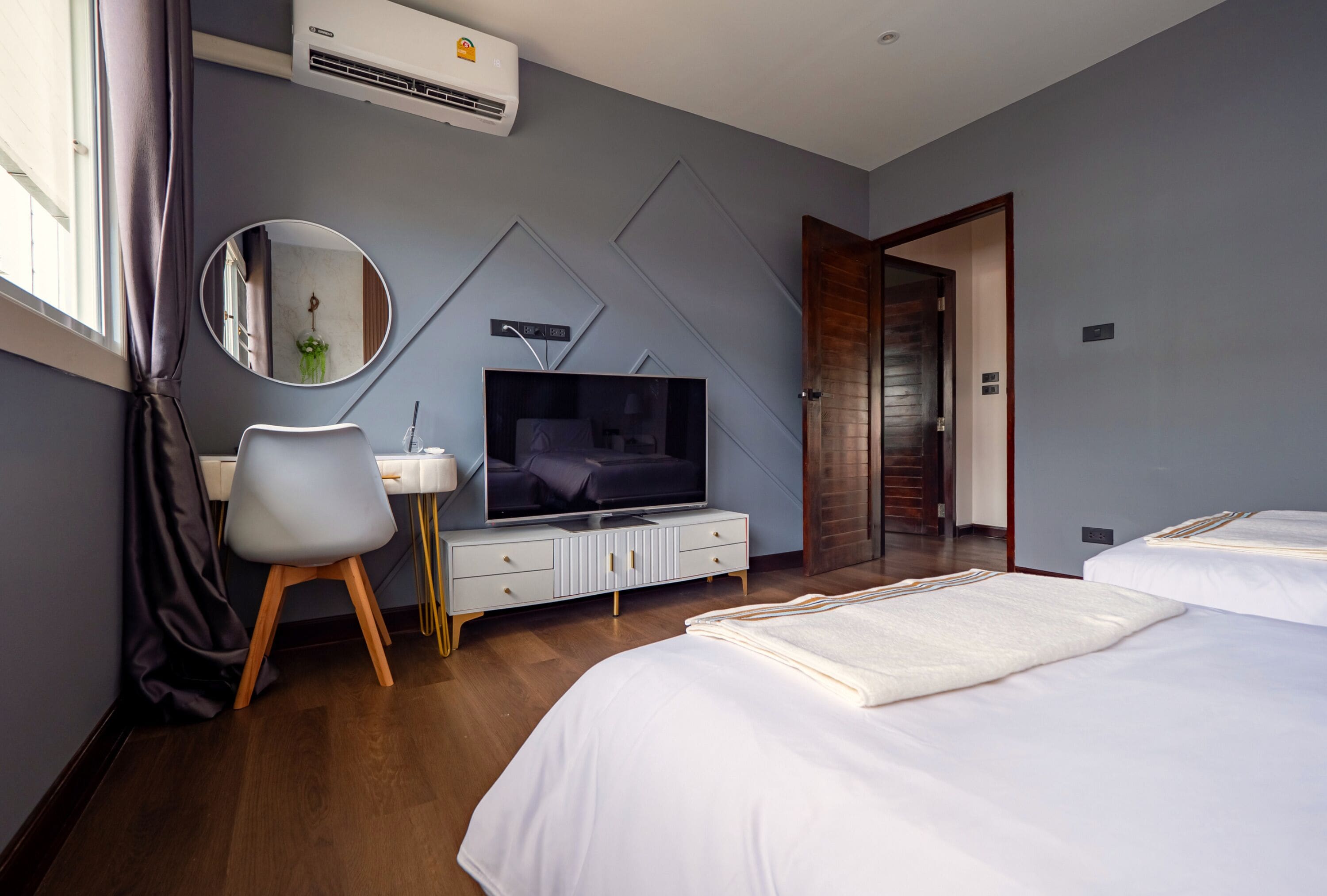 Una habitación de hotel moderna con una televisión de pantalla plana, un escritorio, una silla, una cama y una puerta que da a otra habitación.