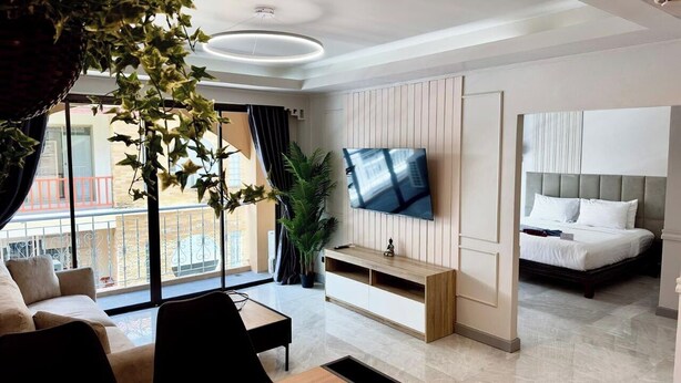 Una habitación de hotel moderna con televisión de pantalla plana, cama, zona de comedor y balcón con vistas.