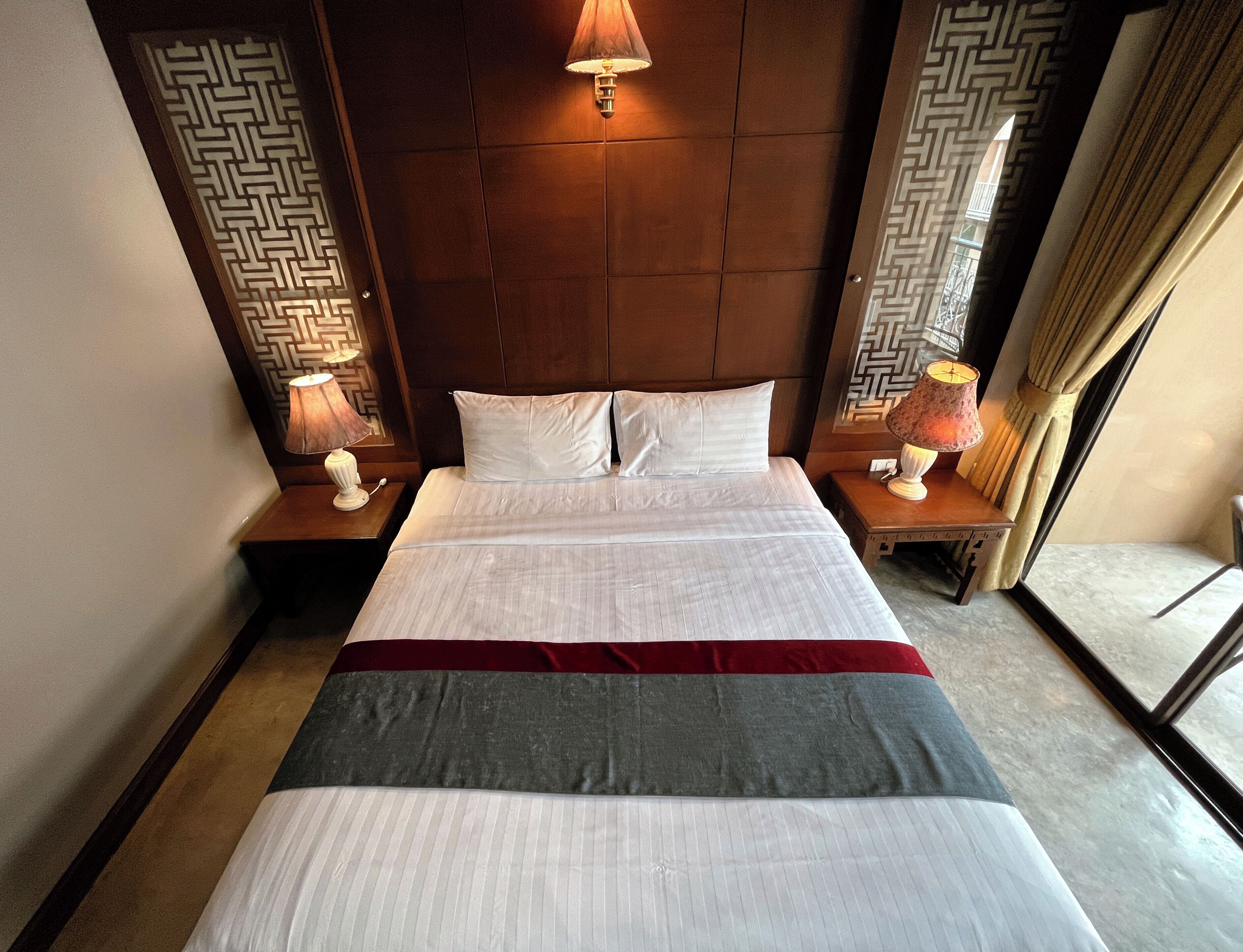 Habitación de hotel con una cama grande, dos lámparas de noche, cabecero y una ventana con cortinas.
