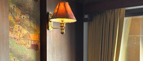 Ett hotellrum med en säng, en väggmonterad lampa, ett stort fönster med gardiner och en dekorativ väggdekoration.