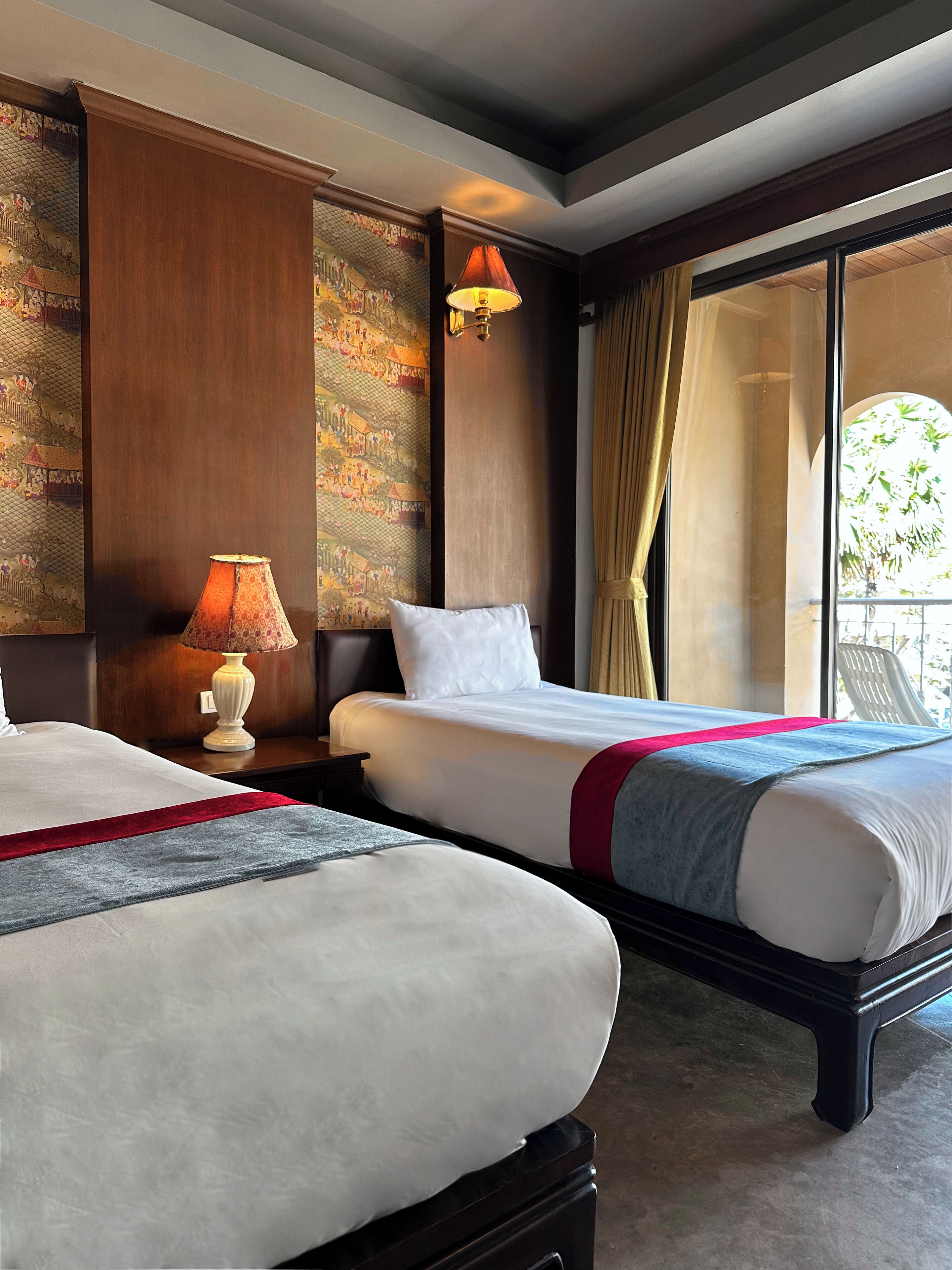 Une chambre d’hôtel avec deux lits, une table de chevet avec une lampe, une grande fenêtre avec des rideaux et une fresque murale.